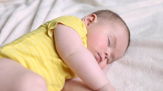 adorable baby boy sleeping on bed.fat hands and legs cute infant toddler with drawn sun from spf uv protection cream.toddler in yellow clothes.summer sun time, skin protection from sun burns.4k