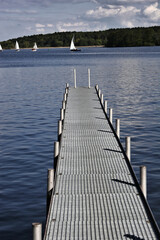 footbridge reaches into a lake with sailing boats in the background