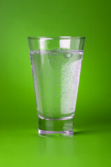 A glass of sparkling mineral water on green background.