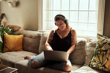 Computer, headphones and woman on sofa and music, happy work from home for mental health in apartment. Young person relax on couch and listening to audio technology, electronics and working on laptop