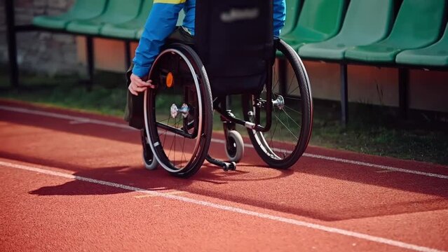 Anonymous Disabled athlete man with defective legs rides in a wheelchair on the street of the stadium outside dressed in sportswear Former athlete