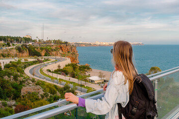 A tourist girl stands on a viewing platform. A girl with a backpack looks at the beach in the city of Antalya.