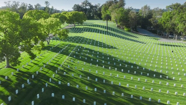 Scenic aerial Los Angeles National Cemetery California USA. Drone flying fast above scenic green field with straight rows white grave plates on summer day. National cemetery where buried armed forces