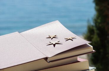 Summertime, vacation, holiday and leisure concept with open book by the sea and three starfish