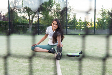 Young woman stretching sitting on floor on padel court with racket 