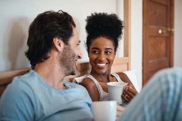 Happy interracial couple, bed and coffee in relax for morning, bonding or breakfast at home. Man and woman smiling for tea, conversation or talk on relaxing weekend or holiday together in the bedroom - obrazy, fototapety, plakaty
