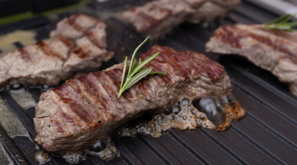 meat beef steak on electric grill cooked, with fresh rosemary. The meat is roasted with stripes. hot photo with steam. grill season
