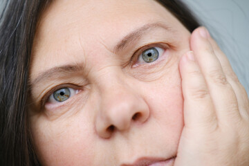 close up part mature female face, woman 50-55 years old looks carefully examines wrinkles around...