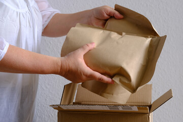 closeup of female hands take out package from open cardboard box, bundle of collagen, postal box with wrapping paper, parcel, delivery of ordered goods, online shopping, timely delivery to customers