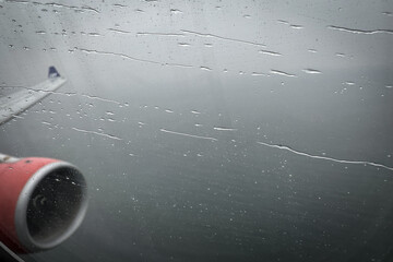 Defocused view on airplane wing through passenger window with rain drops