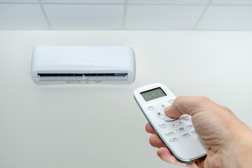 Fototapeta premium HAND ADJUSTING AIR CONDITIONER TEMPERATURE WITH REMOTE CONTROL. ENERGY SAVING AND EFFICIENCY. ENERGY POVERTY CONCEPT.