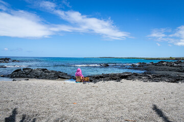 Photo of a woman in a bikini with a bright pink wrap covering her head from the sun on an empty beach on the Big Island of Hawaii.