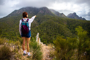 Naklejka premium Beautiful girl points to mighty, famous Mount Barney covered by clouds from Yellow Pinch Lookout, Mount Barney National Park, Brisbane, Queensland