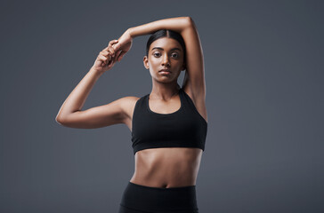 Portrait, mockup space and stretching with a woman in studio on a gray background for exercise or health. Fitness, workout and warm up with an attractive young female athlete training her body