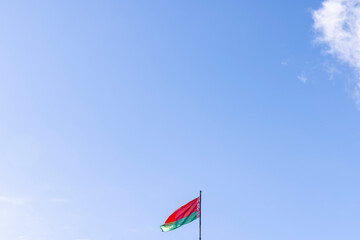 the flag of the Republic of Belarus on a blue sky background with clouds in windy weather