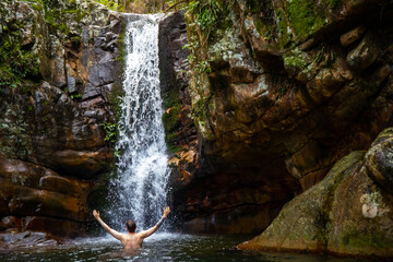 young man with beard and tattoos swimming in the rock pool under large tropical waterfall in mount barney national park, queensland, australia; hidden waterfall in the rainforest