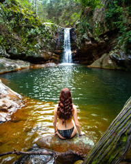 beautiful long hair woman in bikini sitting on the edge of a rock pool in front of large tropical...