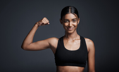 Portrait, smile and woman flexing muscle in studio isolated on black background. Strong, happy and...