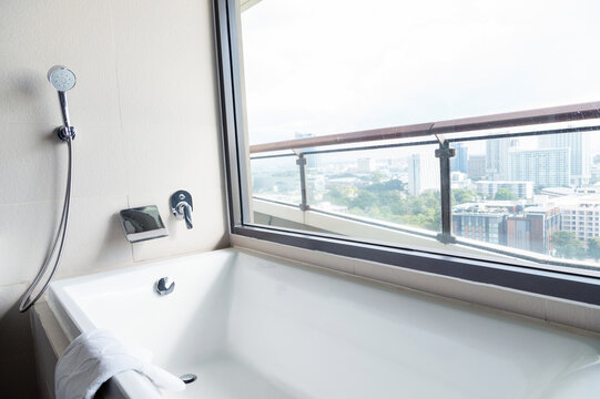 Interior view from bathroom with bathtub and window looking out to big city and high rise luxury hotel buildings. Architect and travel destination concept.