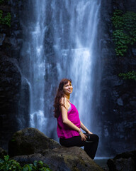 beautiful girl sitting in front of large tropical waterfall - larapinta falls in lamington national park near gold coast, queensland, australia