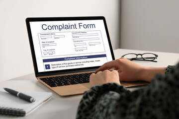 Woman filling online complaint form via laptop at table, closeup