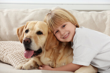Cute little child with Golden Retriever on sofa at home. Adorable pet