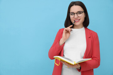 Happy young intern with notebook and pen on light blue background. Space for text