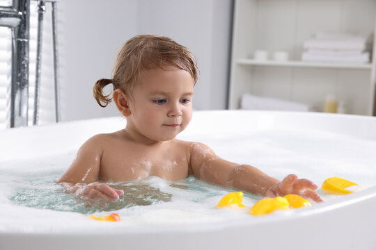 Cute little girl with rubber ducks in foamy bath at home