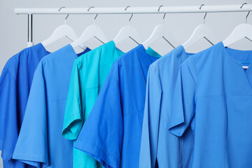 Different medical uniforms on rack against light grey background