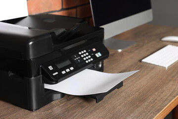 Modern printer with paper near computer on wooden desk at home