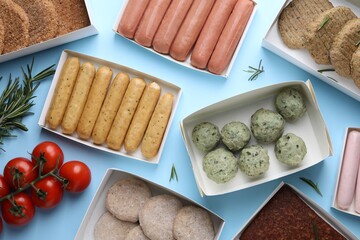 Many different raw vegan meat products, rosemary and tomatoes on light blue background, flat lay