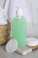 Fototapeta na wymiar Bottle of face cleansing product and cotton pads on light grey table
