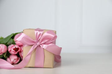 Beautiful gift box with bow and pink tulip flowers on light table, space for text