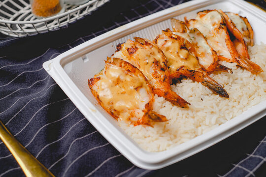 giant shrimp topped with the sauce over rice in take away box for online food delivery and online order.
