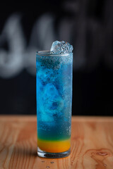 Blue Lagoon mojito. A Mocktail drink which is soda and blue in colour served with ice cubes and fresh orange. Set at cafe on black background and wooden table