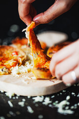 Mini pizzas, vegetarian pizzas with the addition of tomatoes, mushrooms, olives, cheese and fresh herbs on a black background. Side view and added hands