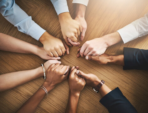 Circle, solidarity and people holding hands by table at group counseling or therapy session. Gratitude, trust and friends with intimate moment for prayer together for religion, unity and connection.