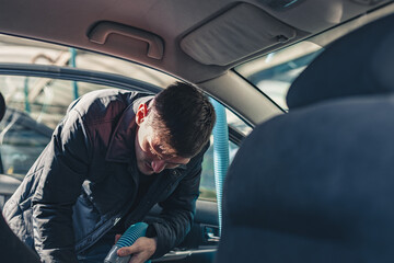 A young man vacuums the interior of a car.