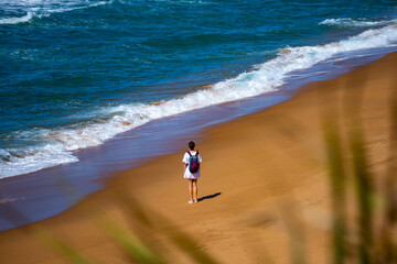 aerial view of beautiful girl with backpack walking lonely on australian beach in deepwater national park near agnes water and town of 1770, queensland, australia; red sand beach in gladstone region