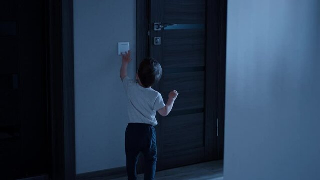 Toddler runs up to the light switch, turns it on and enters the bathroom. Kid takes a prop, stands on it and opens water.