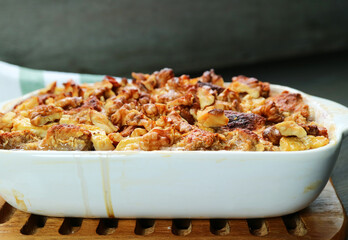 Closeup of Freshly Baked Banana Walnut Bread Pudding in Ceramic Bowl on a Wooden Breadboard