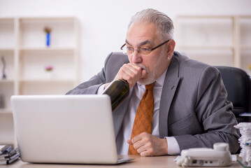 Old male employee drinking alcohol at workplace