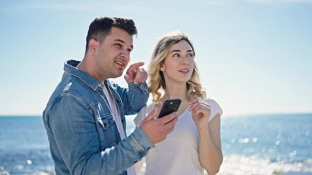 Man and woman couple standing together using smartphone at seaside