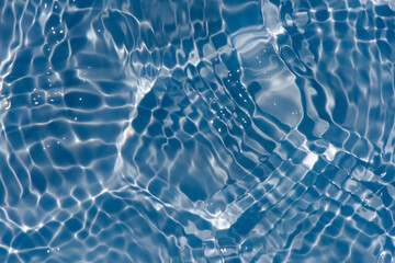 Blue water with ripples on the surface. Defocus blurred transparent blue colored clear calm water surface texture with splashes and bubbles. Water waves with shining pattern texture background.
