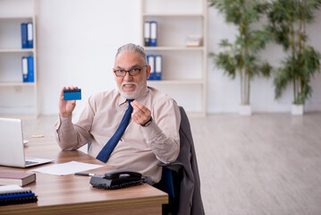 Old male employee holding credit card at workplace