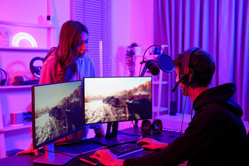 Asian pretty influencer girl looking at computer screen and pressure his boyfriend about playing shooter game in gaming room