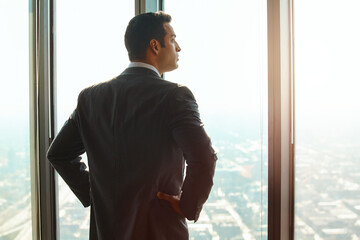 Business man, office window and thinking of ideas, plan or vision with cityscape. Professional male executive with hands on hips for opportunity, dream and future corporate development from behind