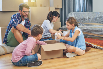 Fototapeta na wymiar Family, kids and moving with boxes for apartment as an investment for lifestyle together in a house. Children, box and parents in living room of a new home are packing for the mortgage for saving.