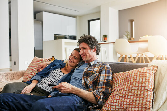Happy couple, relax and watching tv on living room sofa for news, cable show and media connection at home. Mature man, woman and hug with television remote, video subscription and streaming platform
