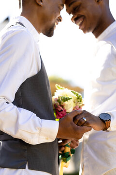 Midsection of african american newlywed gay couple with face to face holding hands with bouquet